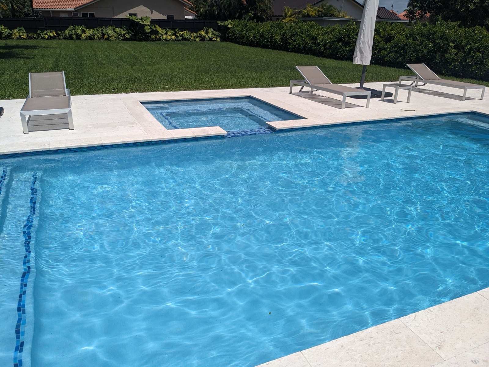 Rectangular pool with attached spa and lounge chairs on a travertine deck